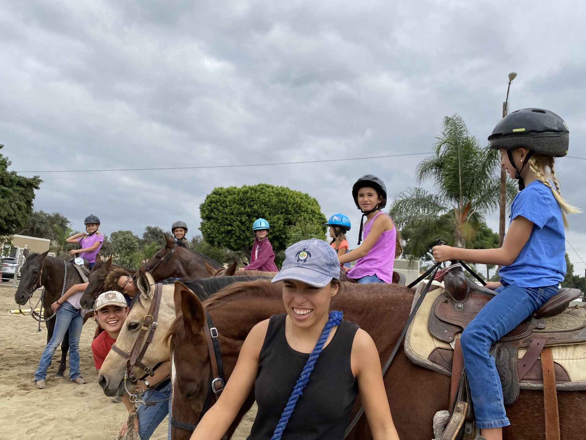 Young riders in helmets on horses at the ranch, a smiling adult in the foreground
