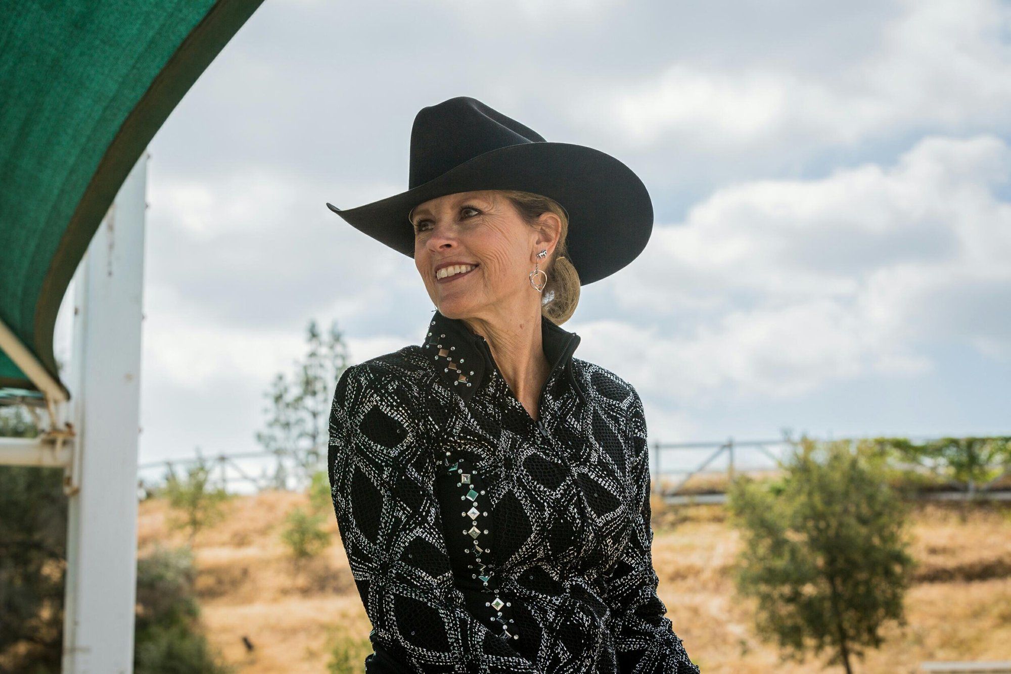 A rider in a black patterned western shirt and black hat, looking off to the side