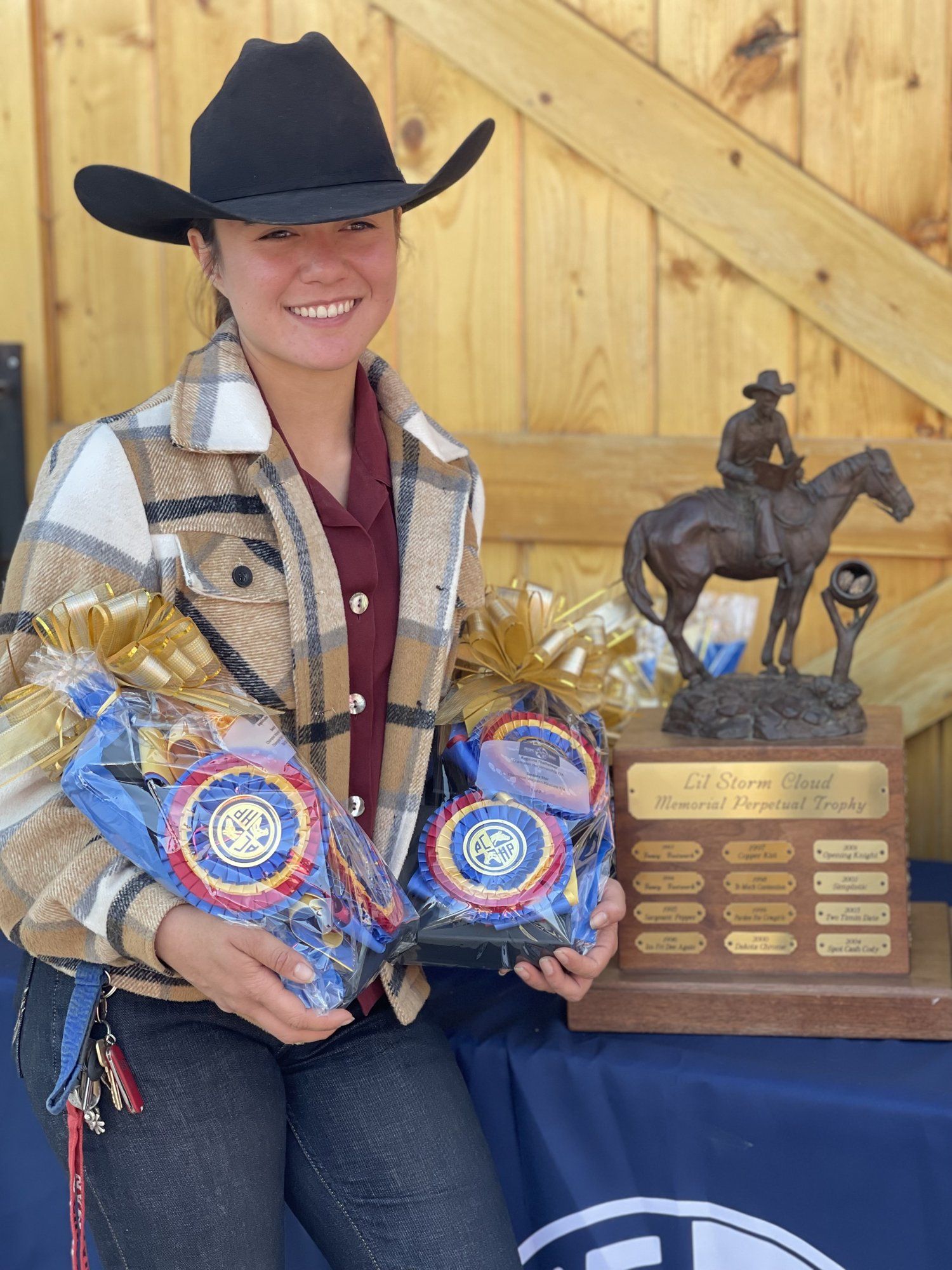 A rider in a black cowboy hat holding two ribbons beside a bronze horse-and-rider trophy
