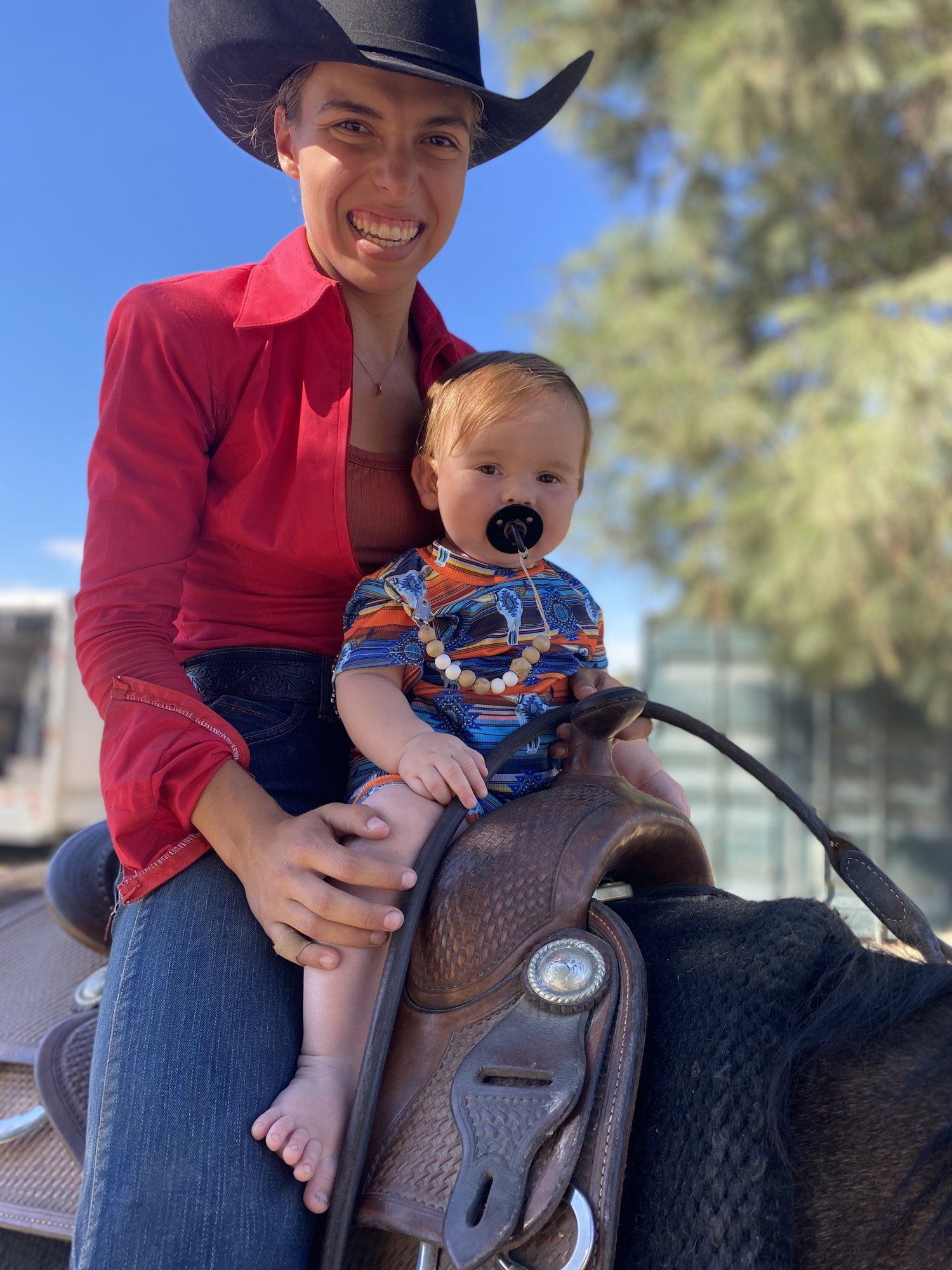 Hayley Bloomquist on horseback in a red western shirt, holding her baby son on the saddle